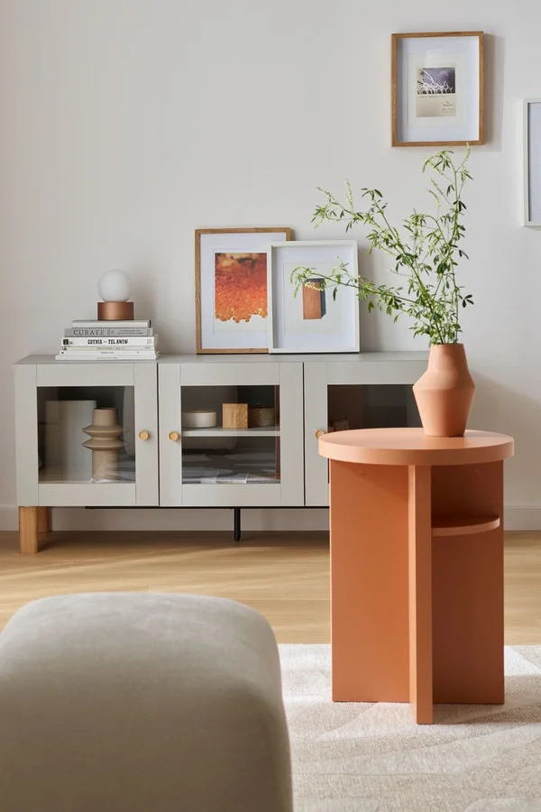 Jasna komoda z rośliną w pomarańczowej donicy i galerią ścienną.